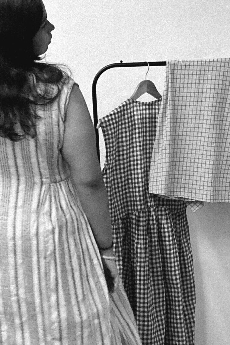 Woman standing beside hanging cotton garments, black and white