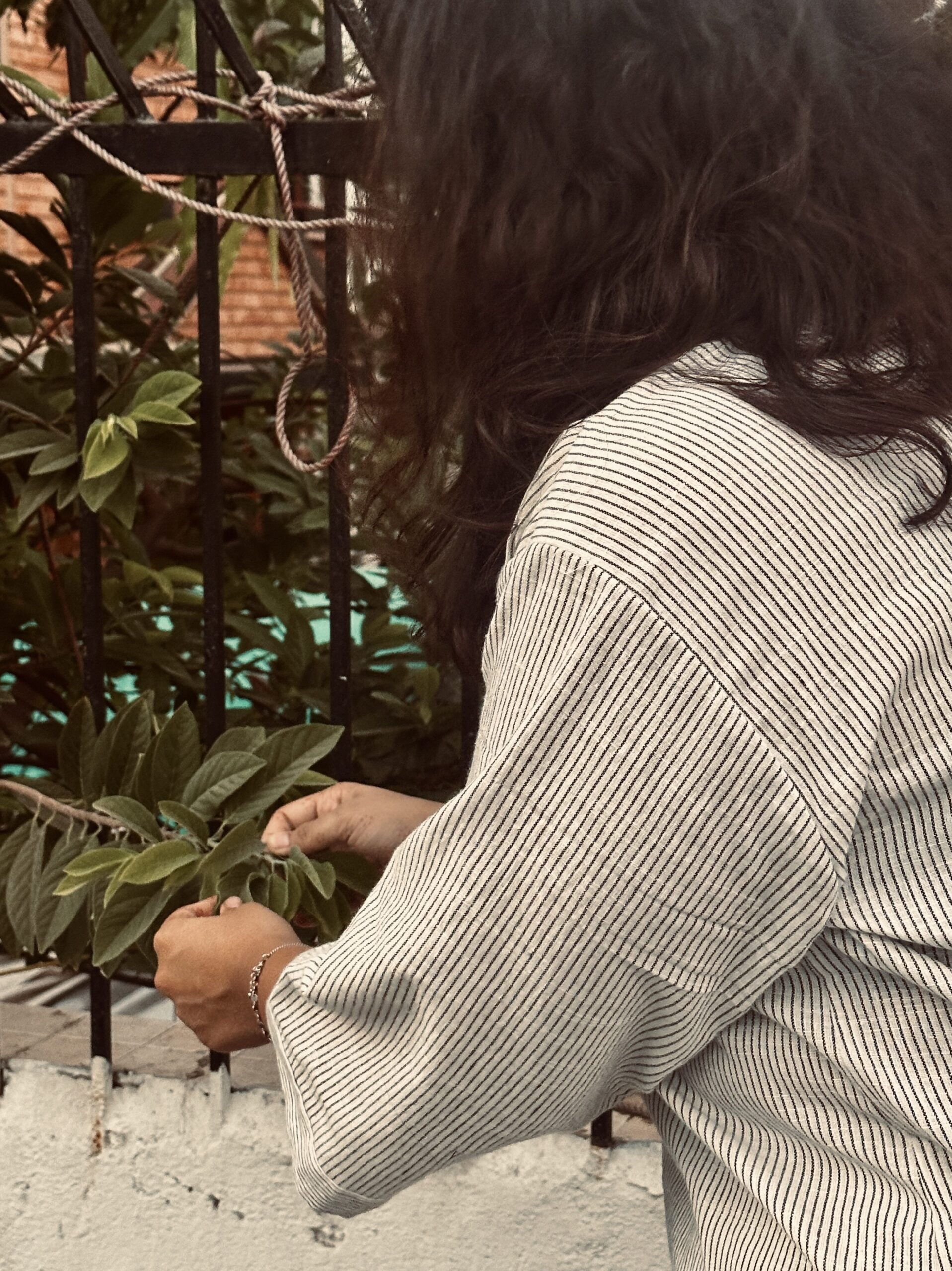Woman in oversized striped cotton shirt tending to plants on a balcony